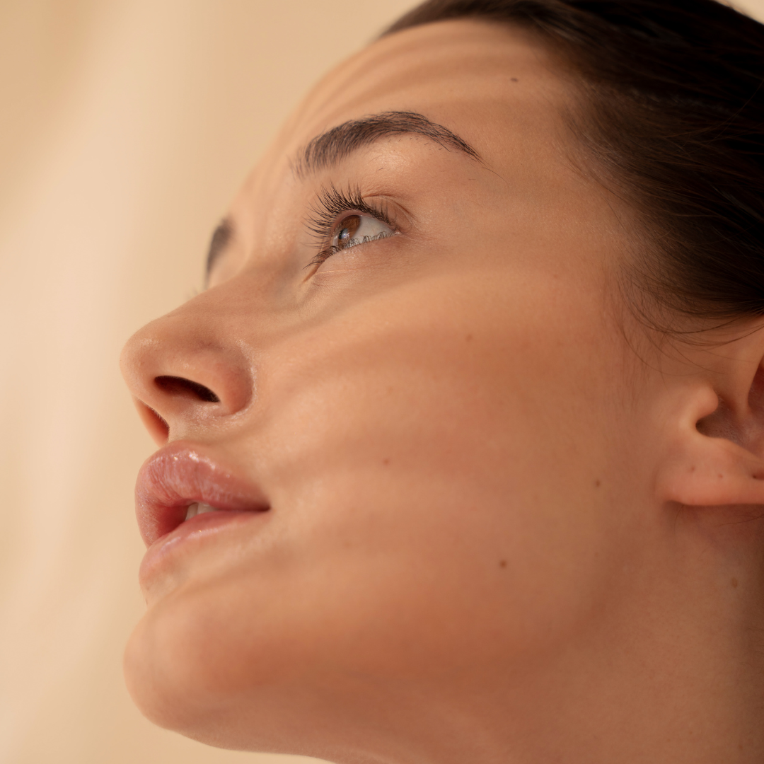 Soft profile view of a woman with light reflecting across her face — capturing a quiet moment of self-care, reflection, and natural beauty with Mythic Cosmetics.
