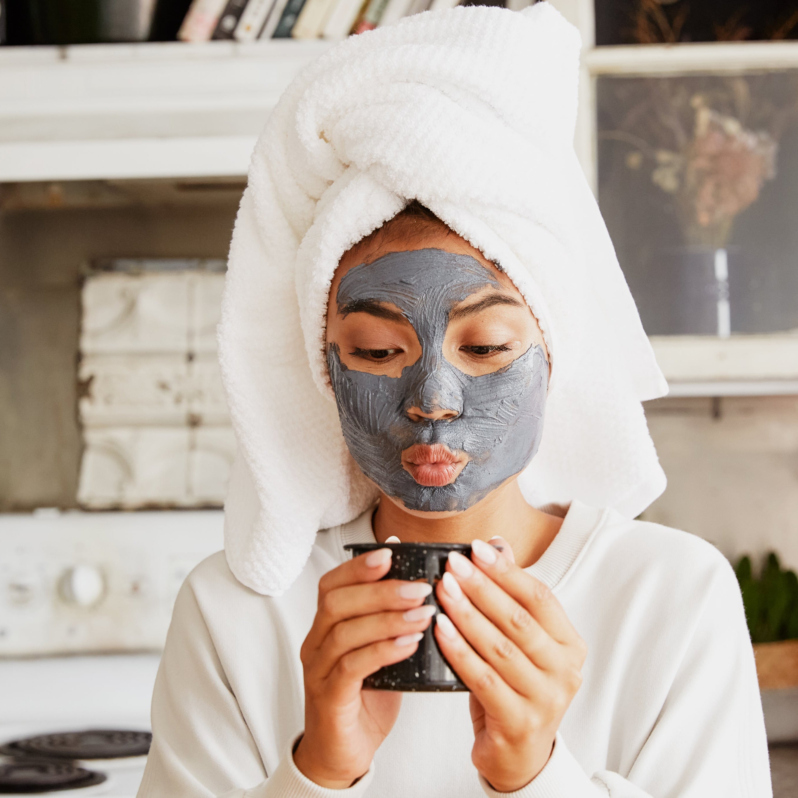 Woman wearing a face mask and sipping coffee — capturing a relaxed, real-life skincare moment with Mythic’s brush-on masks.

